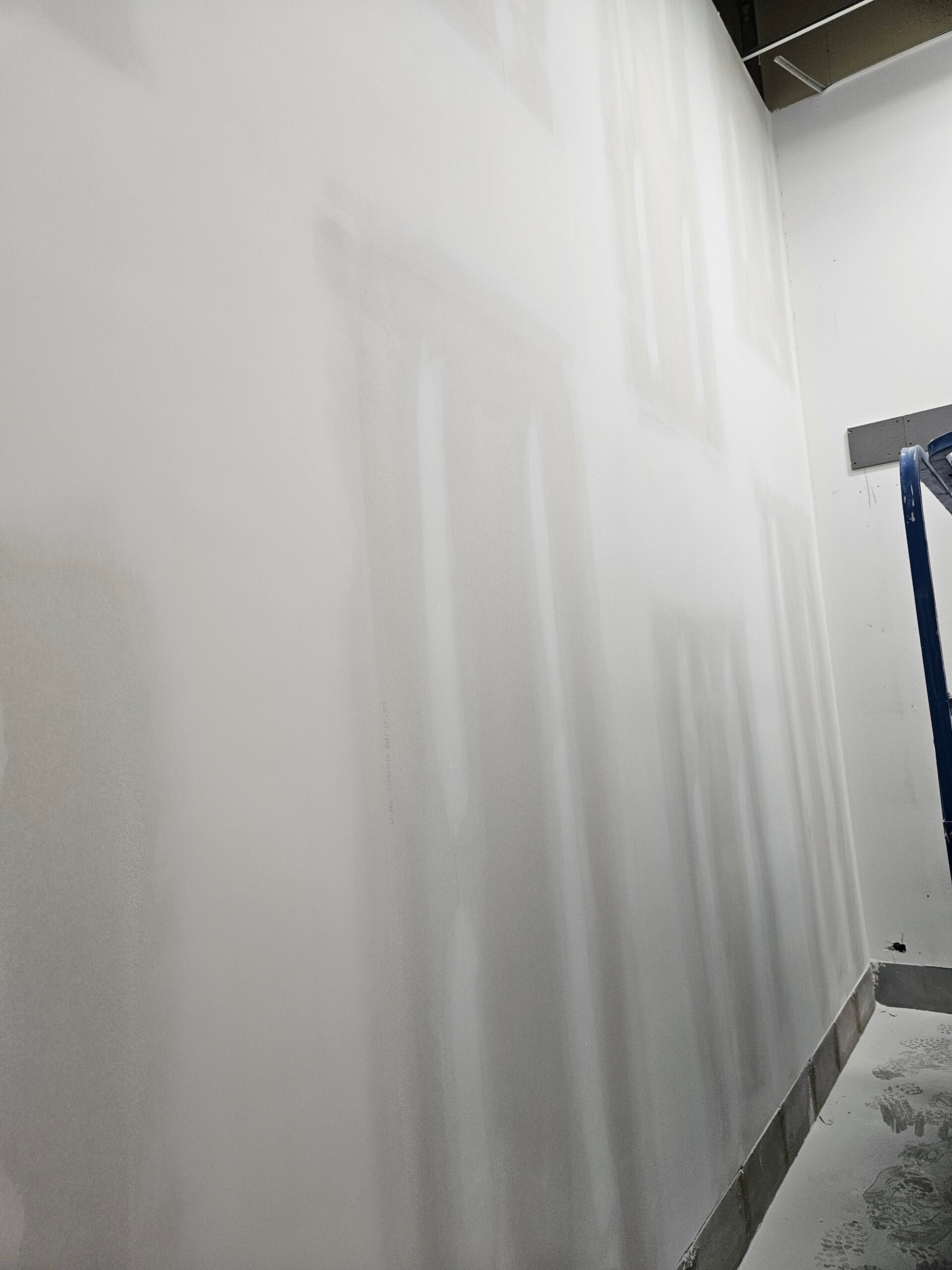 Broad coats of compound along the vertical joints of a tall drywall wall.