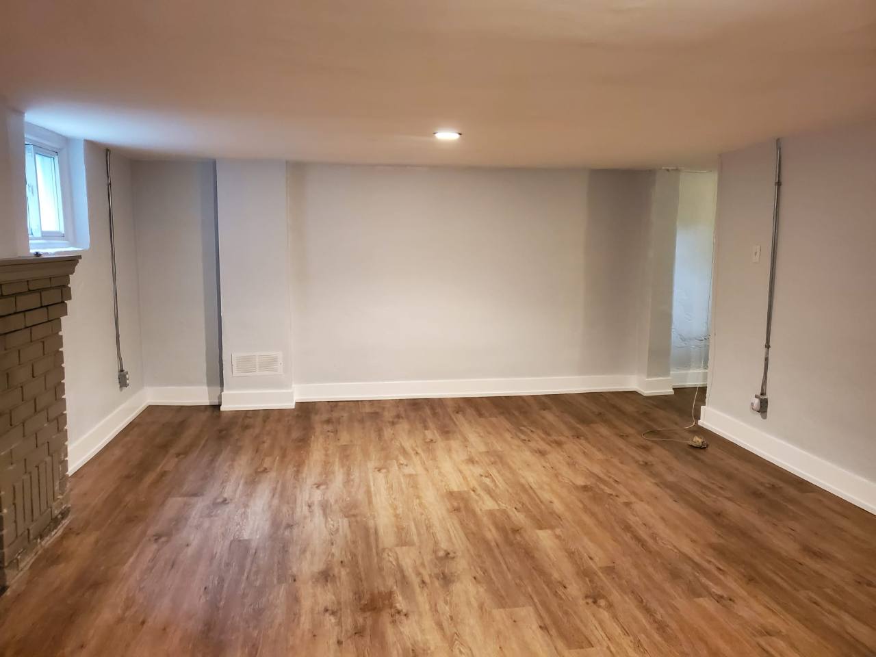 Warm wood-look planks across a basement floor, bordered by white baseboards.