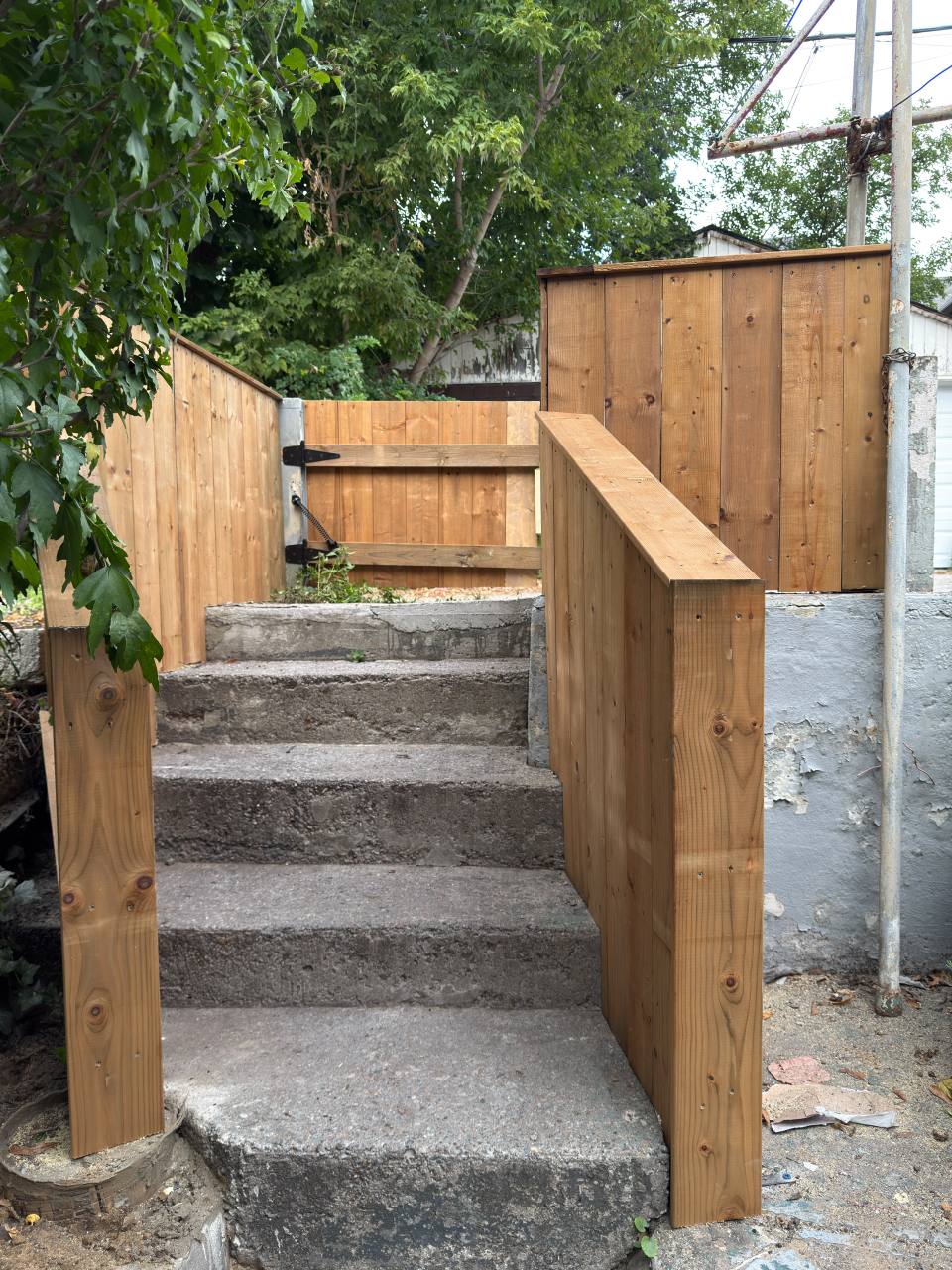Vertical wood boards and wide top caps frame an existing concrete stairway, with a matching gate at the landing.