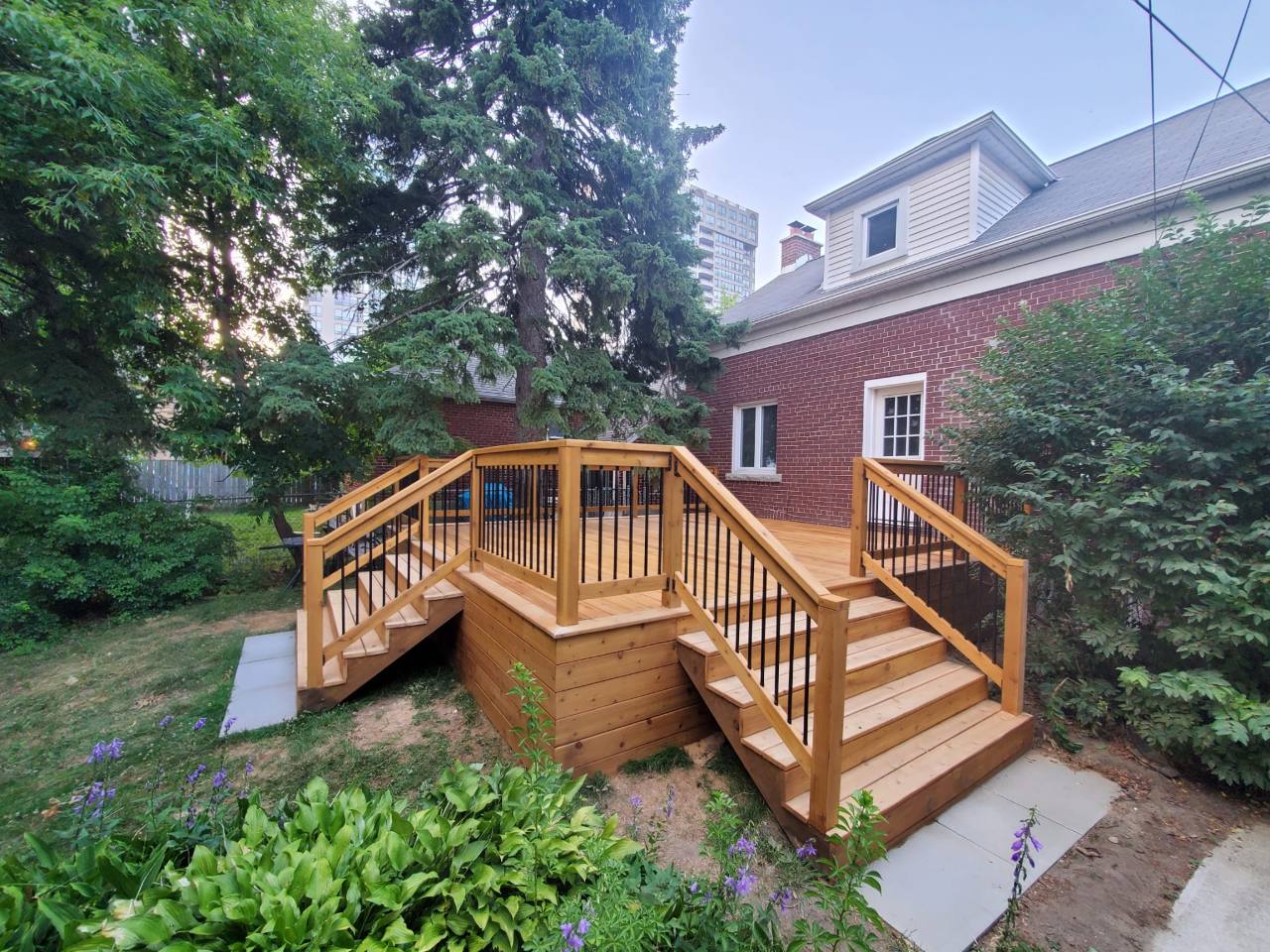 A wood deck with two stairways, black balusters, and horizontal wood skirting beside a brick home.