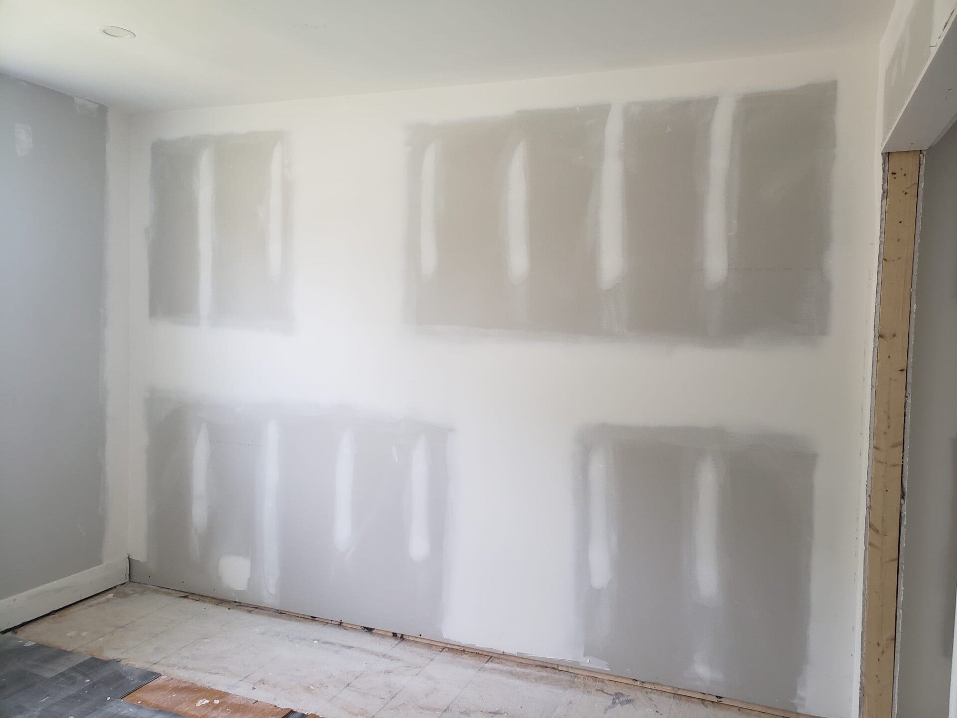 Drywall joints and fasteners covered with compound across an interior wall and its adjoining corners.