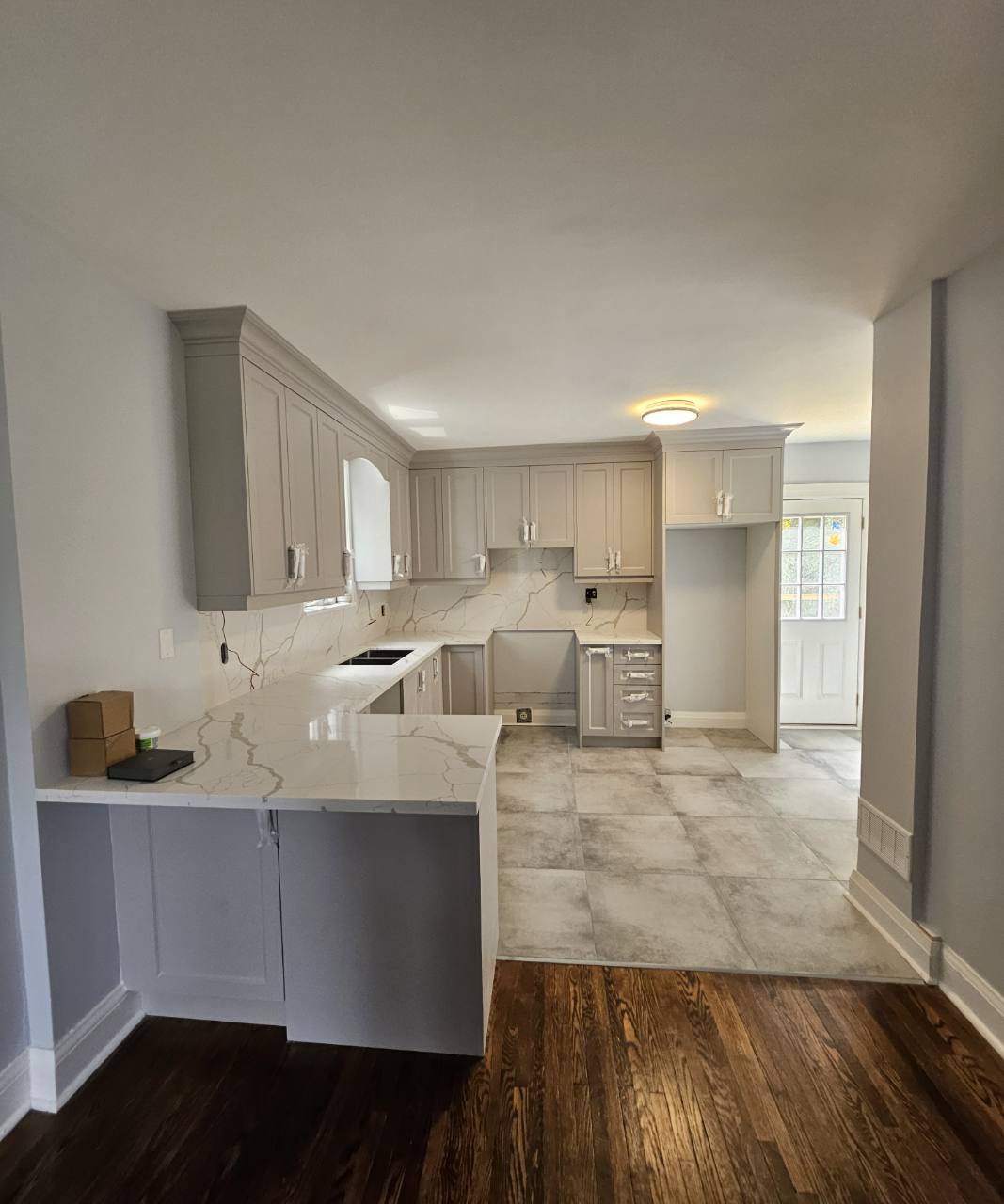 Grey cabinets with a peninsula, veined countertops and backsplash, and a large-format tile floor; appliances and final fittings are not yet installed.