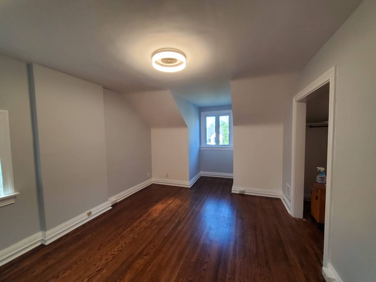 A painted room with light walls, white baseboards, and a window recess beneath a sloped ceiling.
