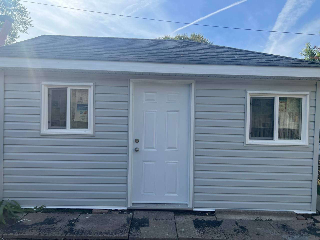 Horizontal light-coloured siding with white trim around the door and two windows.