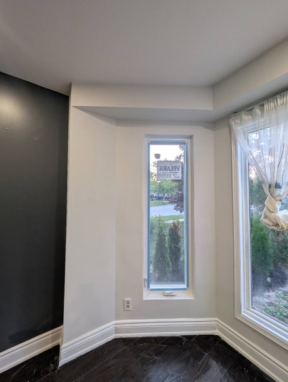 A narrow window with surrounding painted walls, white trim, and baseboards beside a larger window.